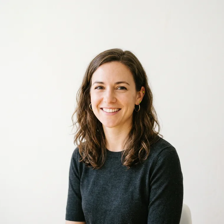 A smiling woman photographed against a plain, brightly lit wall